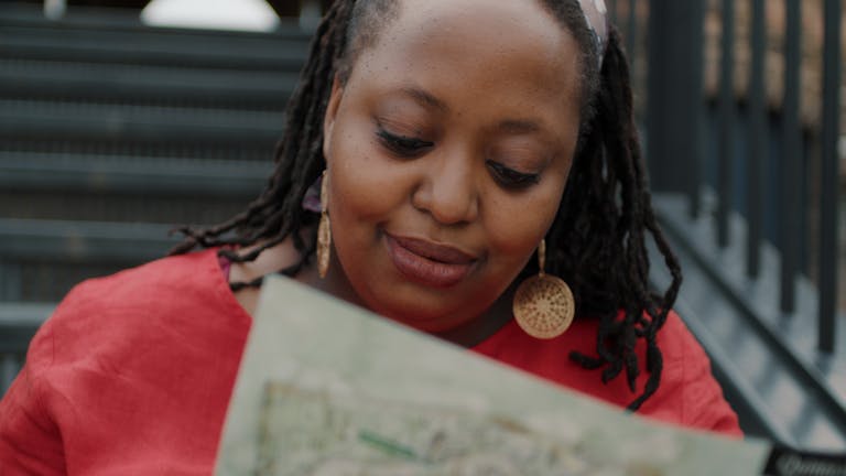 Black woman examining a map while seated on stairs outdoors, deep in thought.