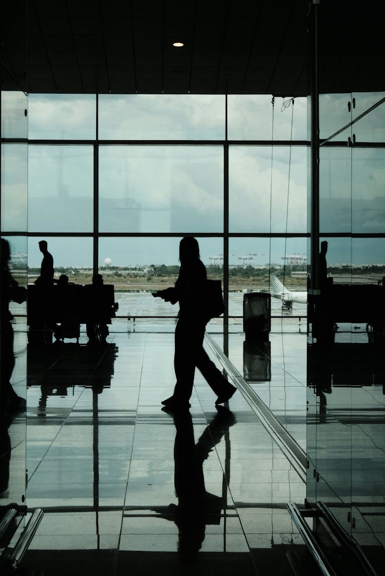 Silhouetted travelers and reflections in Barcelona airport terminal with a backdrop of the runway.
