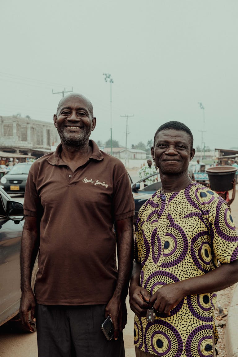Two men standing and smiling on a busy street in Kumasi, Ghana.